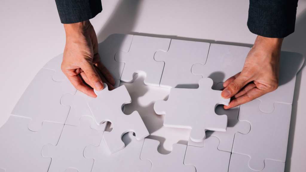 Two hands solving a solid white jigsaw puzzle