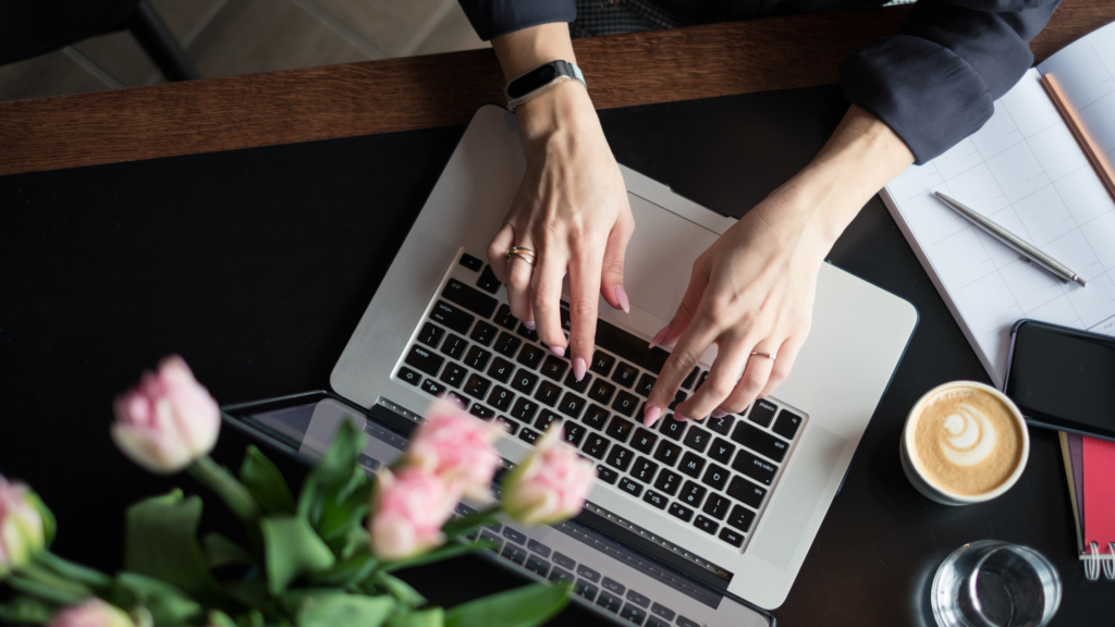 Fingers on a laptop against pink tulips indicating writing skills.